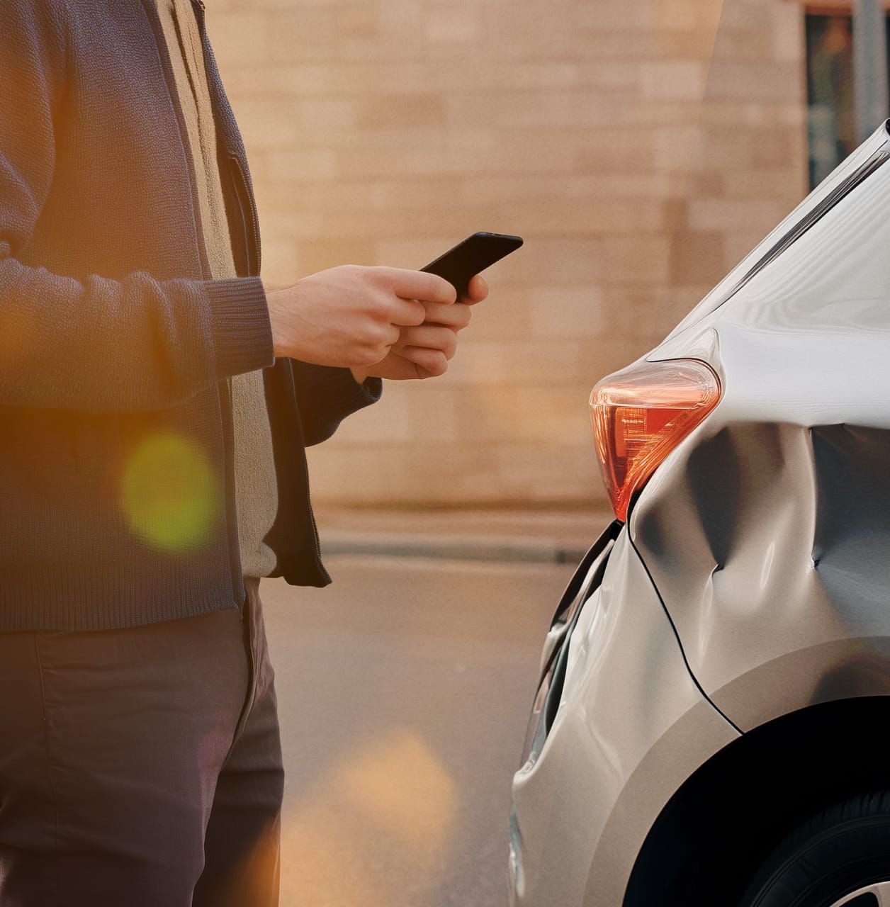 A man using his phone to make a call while standing next to his car